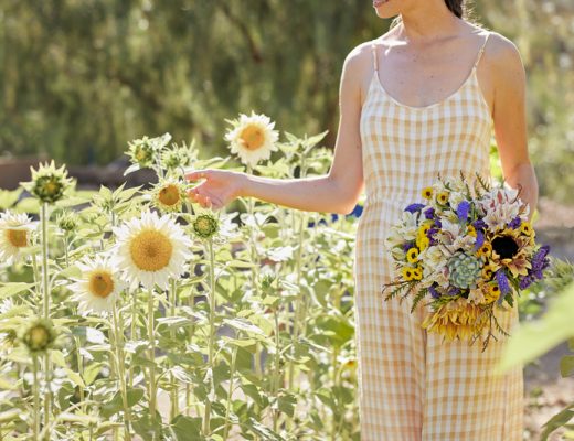 Woman in a yellow and white checked jumpsuit admires sunflowers