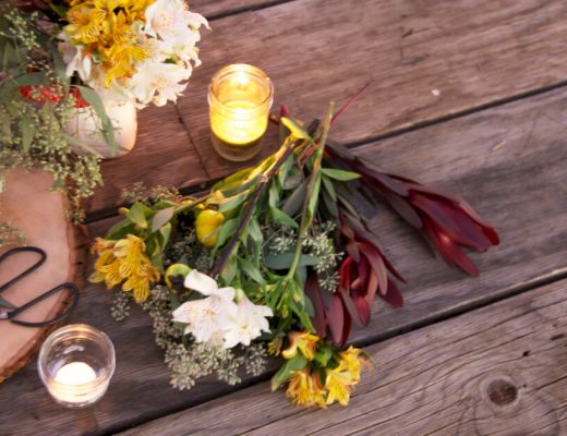 Numerous cut flowers laid out on a table with a candle nearby.