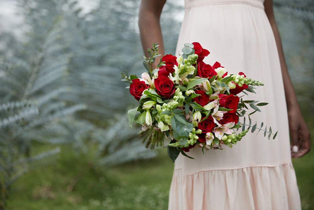 woman holding a bouquet of red roses with greenery
