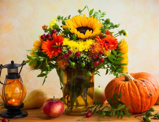 red, flower and green flowers in a vase next to a pumpkin and lantern