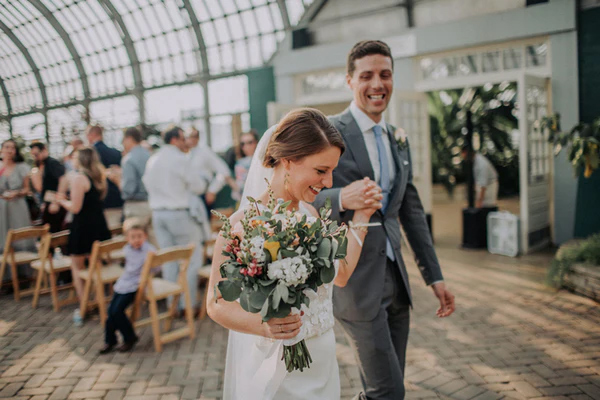 bride walking down the aisle holding a bouquet with yellow and red and white flowers