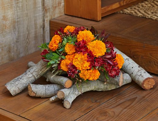 Red and orange flower bouquet display over firewood logs for a rustic arrangement