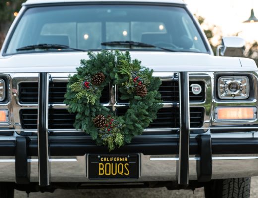 A White Dodge Pickup Truck with a Green Wreath on the Grill and California License Plate that reads Bouqs Ready for Holiday Travel