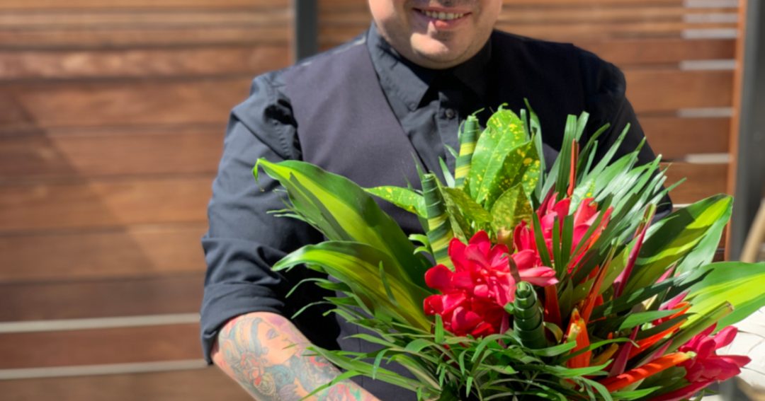 Man Dressed in Black Shirt and Vest Smiling Holding a Tropical Flowers for MenBouquet