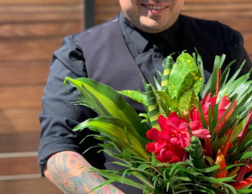 Man Dressed in Black Shirt and Vest Smiling Holding a Tropical Flowers for MenBouquet