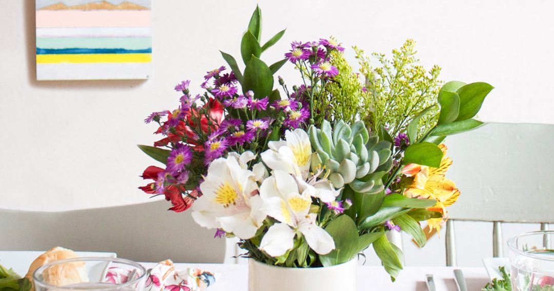 Succulent Bouquet of Cute Flowers in Purple, white, Green and Red in a White Vase on a Table Setting with a Painting in the Background