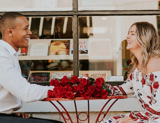Couple laughing at a table with a bunch of red roses.