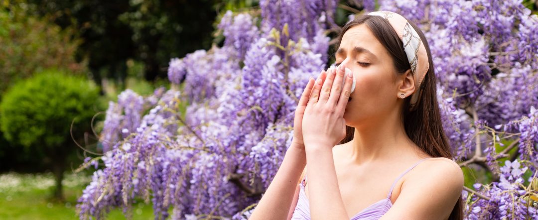 Woman sneezing into tissue near tree of flowers