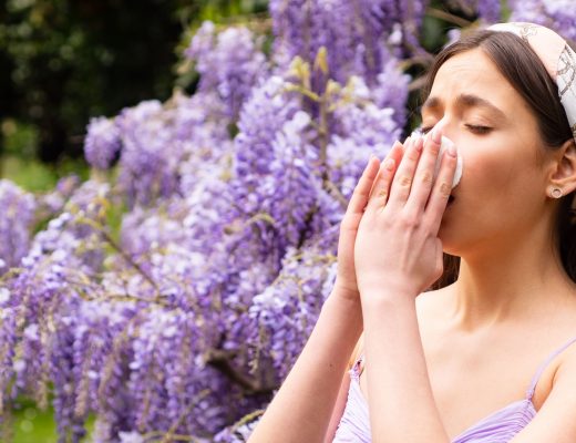 Woman sneezing into tissue near tree of flowers