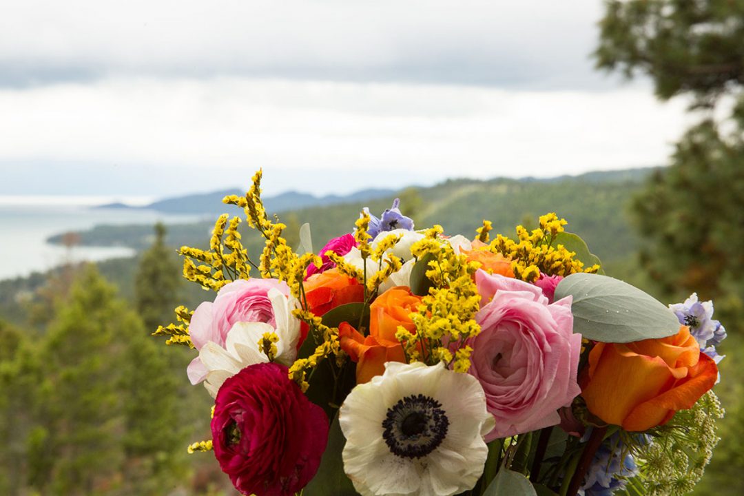 Scenic ocean view in background with red, pink, white, and yellow floral arrangement in foreground.