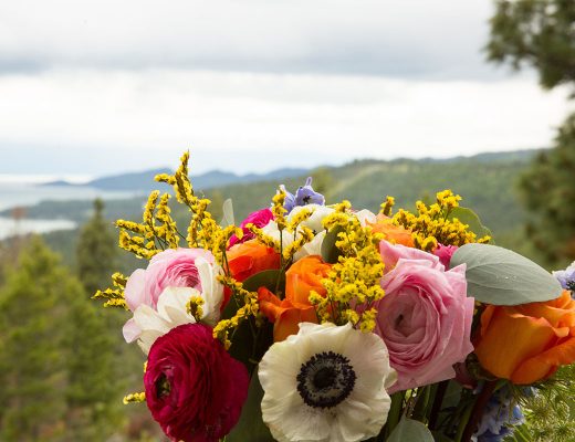 Scenic ocean view in background with red, pink, white, and yellow floral arrangement in foreground.