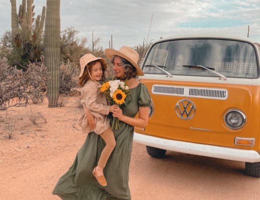 Mother holding daughter and sunflower bouquet with an orange VW van and desert background