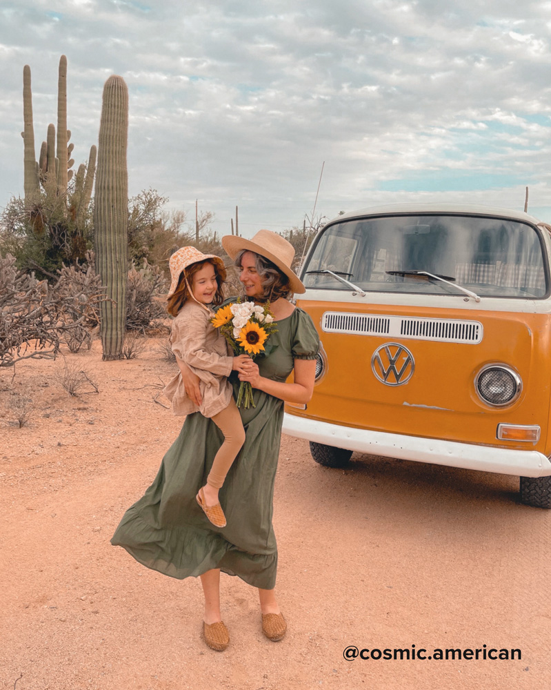 Mother holding daughter and sunflower bouquet with an orange VW van and desert background