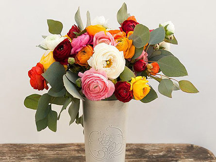 Flower arrangement in red, yellow, pink, and white in vase with eucalyptus filler