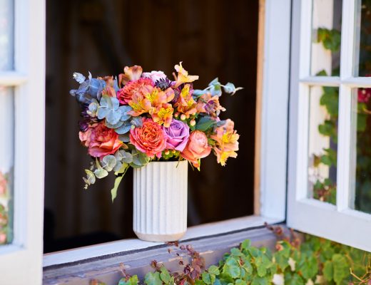 Vibrant orange, purple, peach, and green bouquet sitting in a window designed to showcase the flower's bold colors.