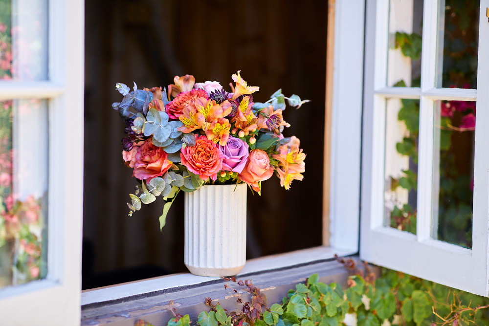 Vibrant orange, purple, peach, and green bouquet sitting in a window designed to showcase the flower's bold colors.