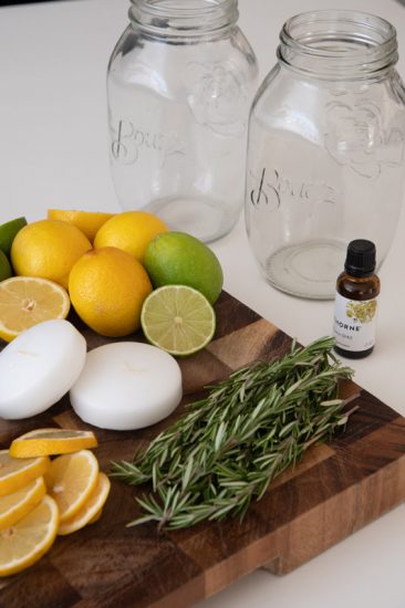 two mason jars, citronella essential oils, rosemary sprigs, lemons and limes, floating candle on a cutting board
