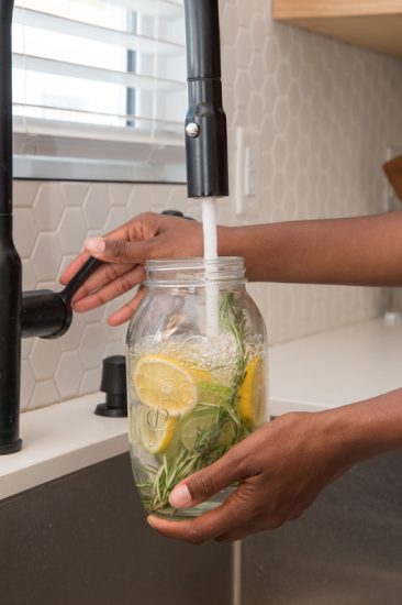 Filling the mason jar with water after lemon and lime slices and rosemary sprig has been placed inside