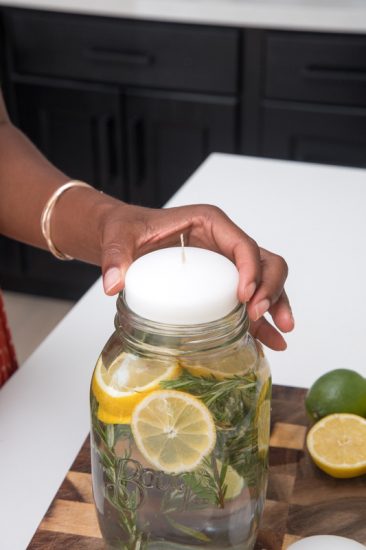 Placing a candle in the mason filled with water, rosemary, citronella oils, lemons and limes