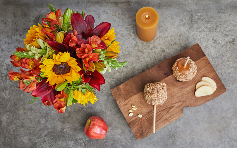 red, yellow, orange flower centerpiece with a candle and candy apples