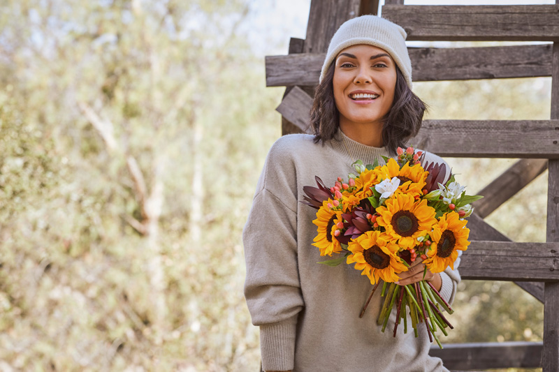yellow sunflower bouquet for friendship held by woman in a beanie and sweater