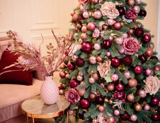 christmas tree decorated with classic sphere ornaments, tinsels, and flowers next to a vase with dried flowers on a table.