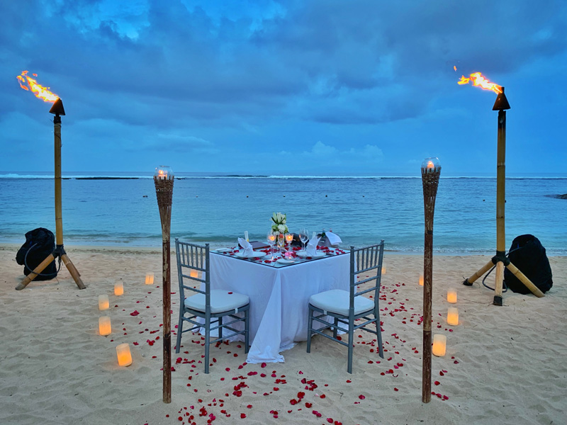 beach date with table torches, flower petals and dinner laid out