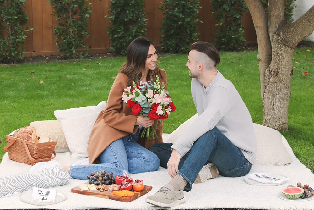couple on blanket in park with flowers having a romantic picnic