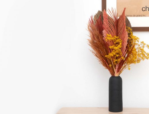 bouquet of dried flowers in a vase against a white wall.