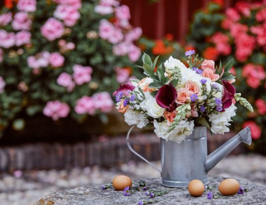 easter flowers in peach, white and burgundy in a tin watering can next to easter eggs