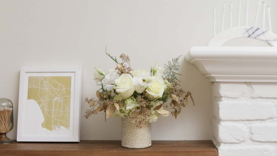 white flowers in a vase on a wood shelf