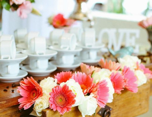 pink and white flowers on a table with white teacups and saucers