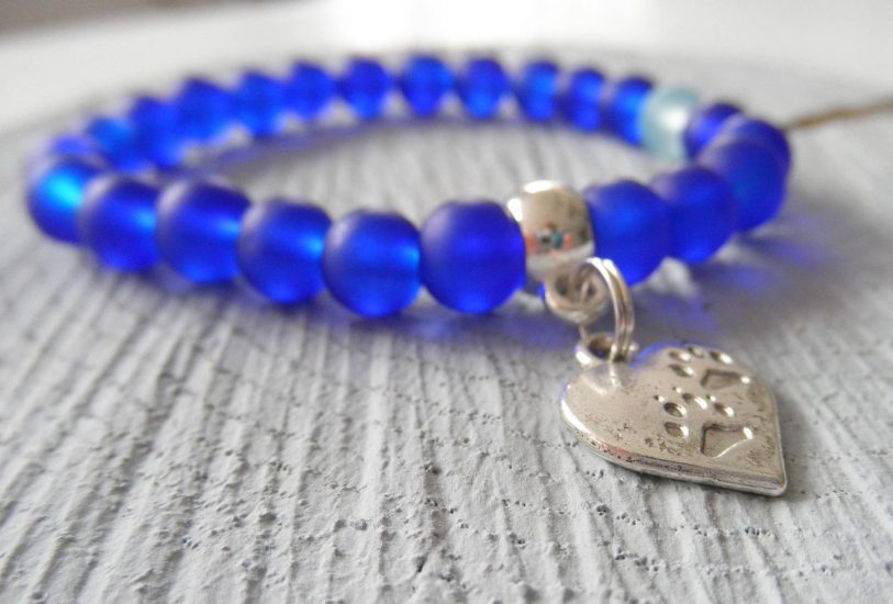 blue beaded bracelet with a heart-shaped metal pendant that has paw prints embedded on it