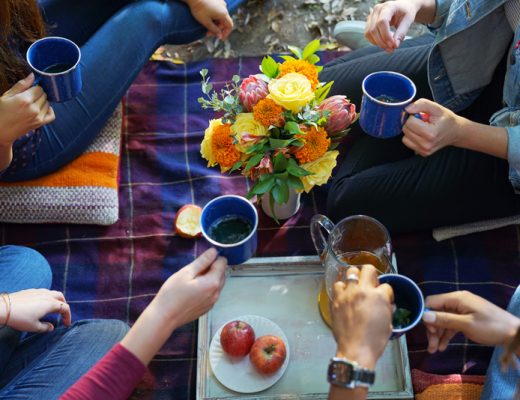 Overhead shot of friends drinking tea with a bouquet of flowers in the middle.