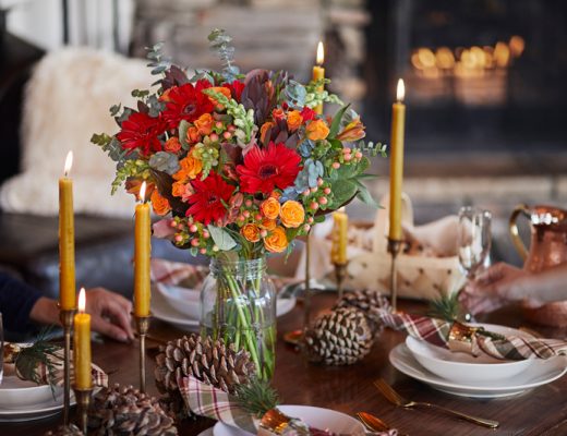 thanksgiving floral centerpiece with red orange and green flowers surrounded by pine cones