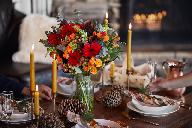 christmas centerpiece with red and orange flowers and pinecones