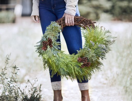 woman holding wreath with pinecones against snowy background