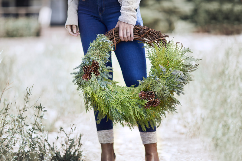 woman holding wreath with pinecones against snowy background
