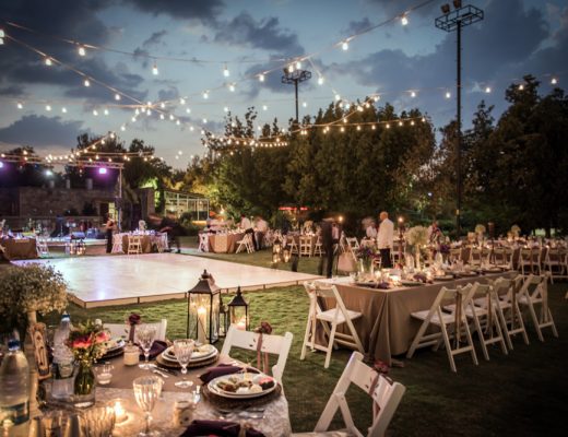 wedding reception tables with hanging lights outdoors on grass