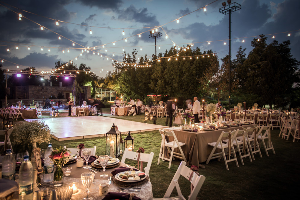 wedding reception tables with hanging lights outdoors on grass