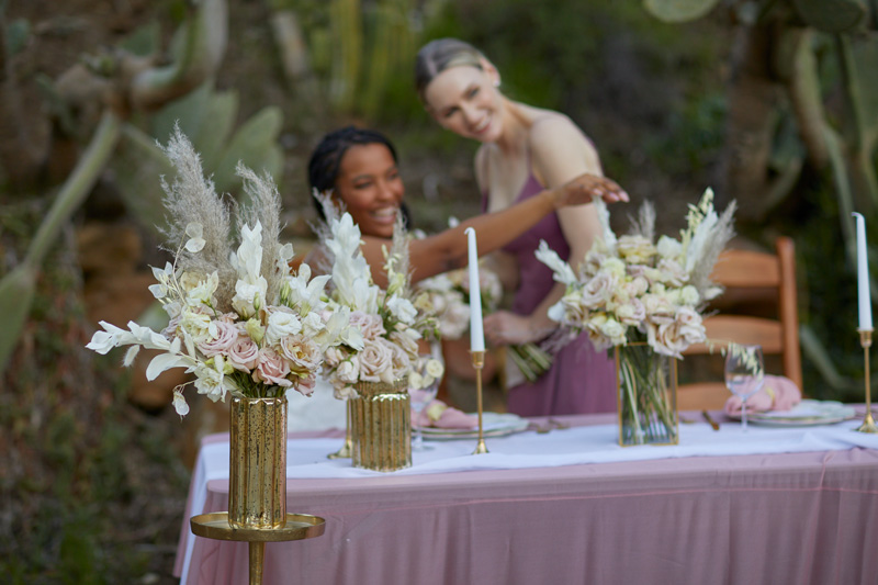 two women celebrating at an event with floral centerpieces in the foreground