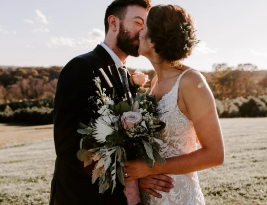 Bride and groom kissing and holding a bouquet of flowers in front of a scenic background