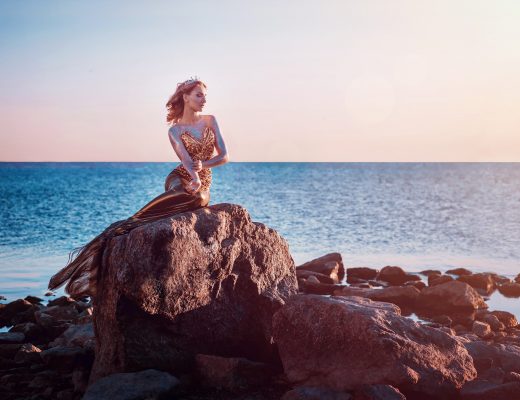 Woman dressed in mermaid-style dress sitting in front of ocean
