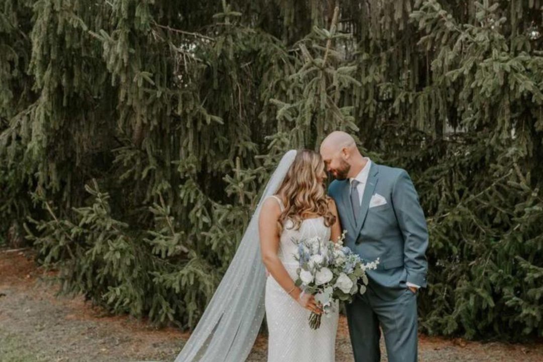 Bride and groom embracing in front of pine trees