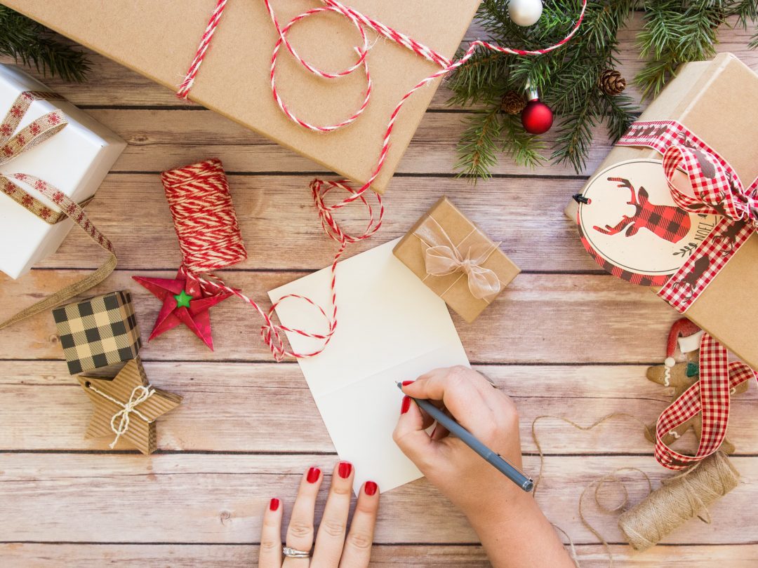 Overhead of someone writing a Christmas card on a decorated table