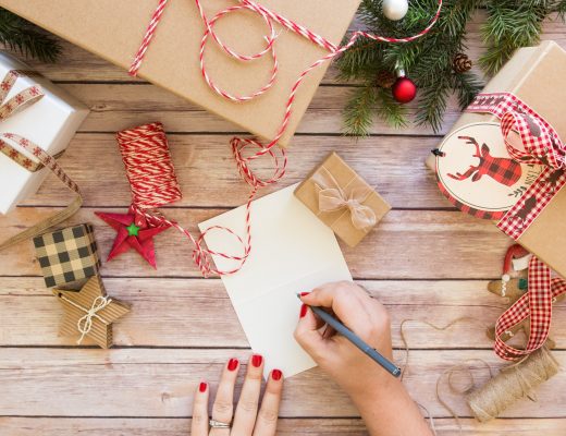 Overhead of someone writing a Christmas card on a decorated table