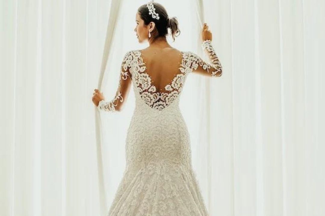 Bride standing next to an open window in her white wedding dress