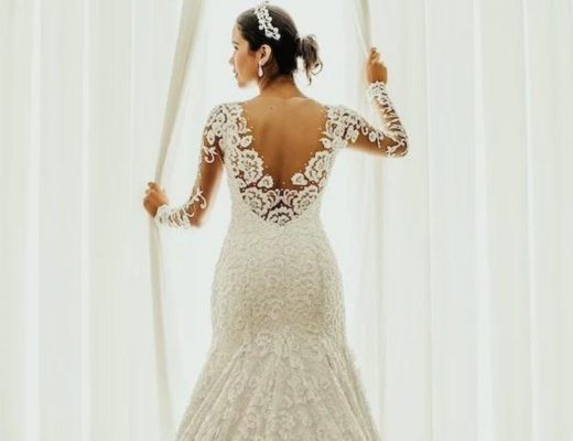 Bride standing next to an open window in her white wedding dress