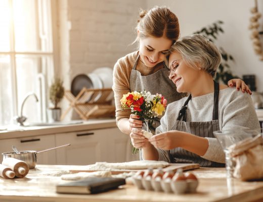 Woman surprising her older mom with flowers while they're prepping to bake.