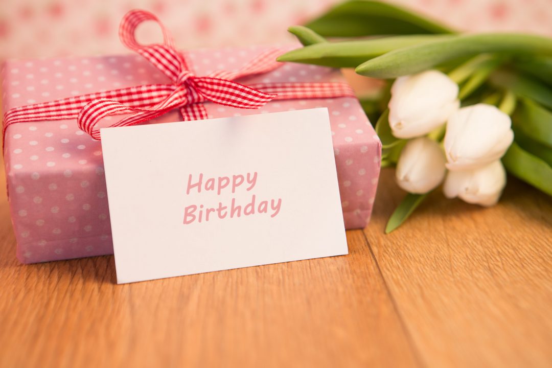 A birthday card, wrapped gift, and white tulips on a table.